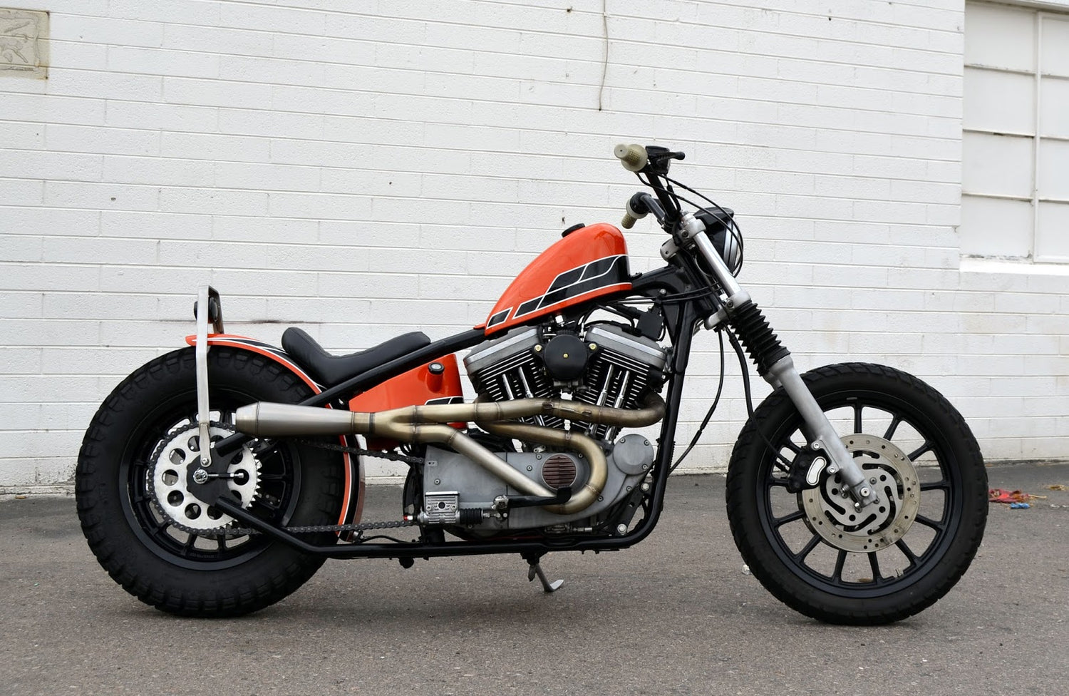 orange sportster chopper in front of white brick wall